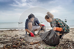 Problems of environmental pollution and oceans, a young couple in orange gloves cleans plastic and garbage in a black trash bag on