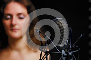 Problems for vocalists and singers when recording songs in a studio. Young woman blur next to microphone on black background