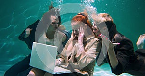PROBLEMS AT WORKPLACE Two angry female bosses shout at young manager using laptop touching head underwater slow motion.