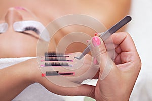 The procedure for eyelash extensions in the beauty salon, eyelashes on the hand of the make-up artist.