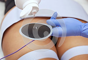 The procedure of myostimulation on the legs and buttocks of a woman in a beauty salon.