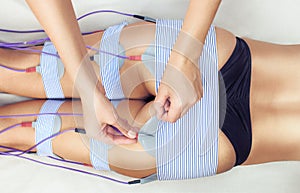 The procedure of myostimulation on the legs and buttocks of a woman in a beauty salon