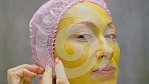 Procedure for skin care to face of young pretty woman. Beauty salon, facial peeling yellow gold alginate mask with