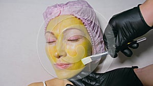 Procedure for skin care to face of young pretty woman. Beauty salon, facial peeling yellow gold alginate mask with