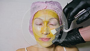 Procedure for skin care to face of young pretty woman. Beauty salon, facial peeling yellow gold alginate mask with