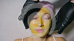 Procedure for skin care to face of young pretty woman. Beauty salon, facial peeling yellow gold alginate mask with