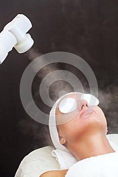 The procedure of steaming the skin of the face of a young woman before cleaning the skin,