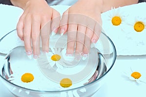 Procedure for treating nails in spa salon. Close-up hands of young woman with natural nails, lowered into plate with healing infus