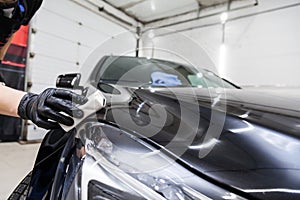 The process of applying a nano-ceramic coating on the car`s hood by a male worker with a sponge and special chemical composition photo