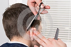 The process of child hair cutting behind the ear with scissors, leveling the length