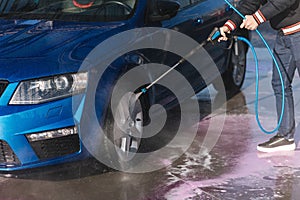 Process of cleaning car with a jet sprayer. Self service car washing. Close-up of man wash wheels