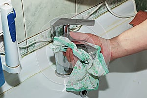 The process of daily cleaning the sink with washing powder and household rag. A housewife with hand without glove cleans the water