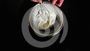 The process of cooking with eggs. The cook whips the batter with a whisk. Egg yolk, milk, stainless steel plate.