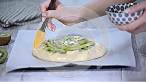 The process of cooking a galette with fresh kiwi. Female chef lubricate the bakery products with an egg.