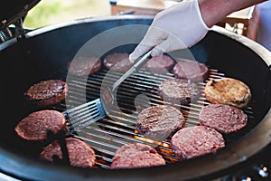 Process of cooking and grilling beef burgers on open-air street food festival, view of chef hands in gloves with variety of