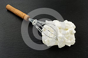 Process of cooking meringue. Whipped egg whites on whisk on slate background. Baking dessert concept