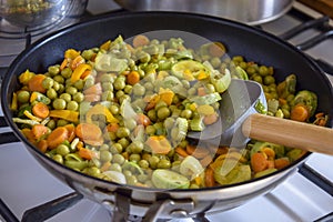 Process of cooking saute at home. Stewed vegetables and silicone spatula with wooden handle in frying pan. Mixed Ingredients