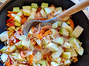 Process of cooking saute at home. Stewed vegetables and silicone spatula with wooden handle in frying pan. Mixed Ingredients