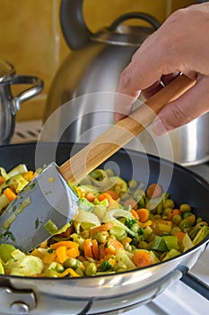 Process of cooking saute at home. Woman`s hand mixed stewed vegetables in frying pan