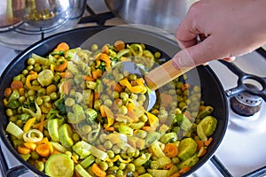 Process of cooking saute at home. Woman`s hand mixed stewed vegetables in frying pan on gas stove with silicone spatula with