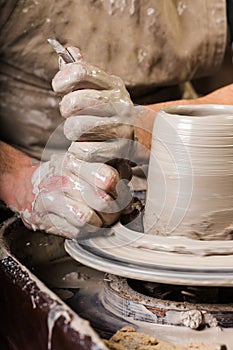The process of creating a pottery on a twisted Potter`s wheel close-up. Dirty hands in the clay and the potter`s wheel