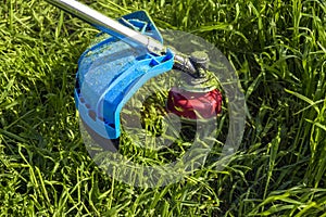 Process of cutting green grass with trimmer. Rotating head with red fishing line cuts grass. Gasoline powered mower. Close-up.