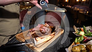 Process of cutting the steak with a large kitchen knife on a cutting board. Rack of beef meat is cut into pieces.