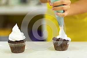 The process of decorating chocolate cupcakes with airy protein cream. Creation of cakes by professional pastry chefs