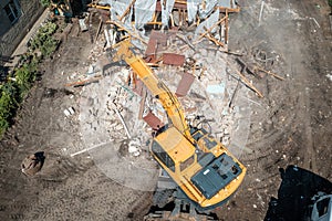 Process of demolition of old building dismantling aerial view. Excavator breaking house. Destruction of dilapidated