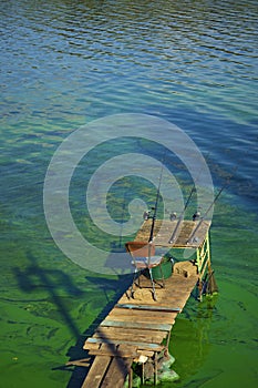 Process of fishing with rods. Wooden deck with three fishing rods beside the lake. Waiting for catching some fish.