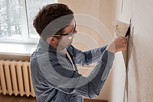 Caucasian man tearing off old wallpaper from wall preparing for home redecoration photo