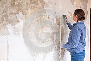 Caucasian woman tearing off old wallpaper from wall preparing for home redecoration photo