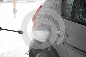 A process of flushing soap sud on silver car with pressurised water stream at self-service indoor car wash station