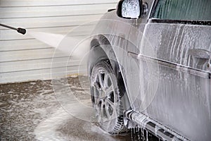 A process of flushing soap sud on silver car wheel with pressurised water stream at self-service indoor car wash station