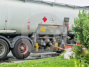 Process of a fuel transfer from a tank truck into filling station gas reservoir. Side view of tank track and connected hose