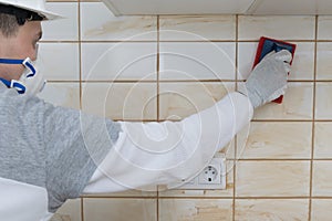 The process of grouting cracks, tiles on the wall with a spatula with a sponge, a master in protective clothing