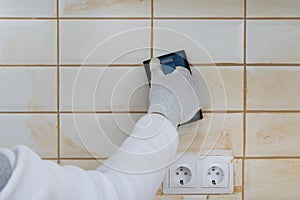 The process of grouting cracks, tiles on the wall with a spatula with a sponge, a master`s hand in protective clothing, close-up