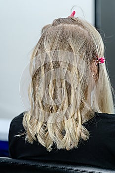 Process of hairstyling with curler for blond woman after hair bleaching