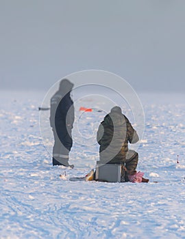 Process of ice fishing, group of fishermen on ice near tent shelter, with equipment in a winter snowy day, tents and ice auger on