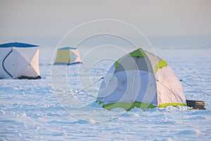 Process of ice fishing, group of fishermen on ice near tent shelter, with equipment in a winter snowy day, tents and ice auger on