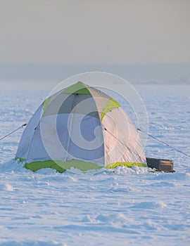 Process of ice fishing, group of fishermen on ice near tent shelter, with equipment in a winter snowy day, tents and ice auger on
