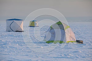 Process of ice fishing, group of fishermen on ice near tent shelter, with equipment in a winter snowy day, tents and ice auger on