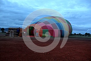 Process of inflation and preparation of hot air balloon at sunrise for flight in cloudy sky