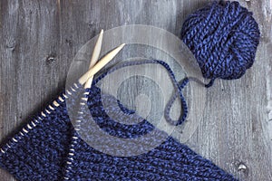 Process of knitting. Ball of blue woolen thread and knitting needle closeup on wooden