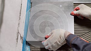 Process of laying ceramic tiles on floor smeared with glue. Workers hands with a tile close up. The process of laying