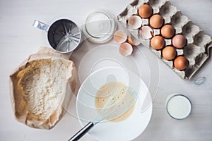 Process of making the dough, woman`s hand whips eggs and flour in bowl Flat lay composition of ingredients and batter.selective