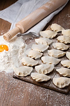 Process of making dumplings, vareniki, pierogi, on wooden board on table with rolling pin, sprinkled with flour and