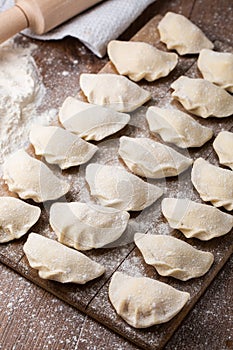 Process of making dumplings, vareniki, pierogi, on wooden board on table with rolling pin, sprinkled with flour and