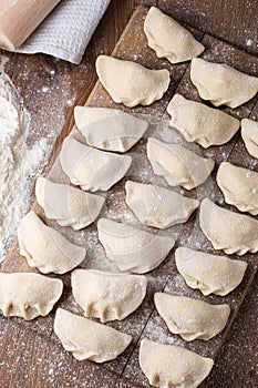 Process of making dumplings, vareniki, pierogi, on wooden board on table with rolling pin, sprinkled with flour and