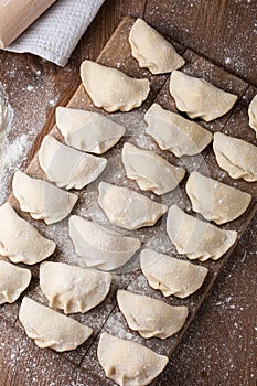 Process of making dumplings, vareniki, pierogi, on wooden board on table with rolling pin, sprinkled with flour and